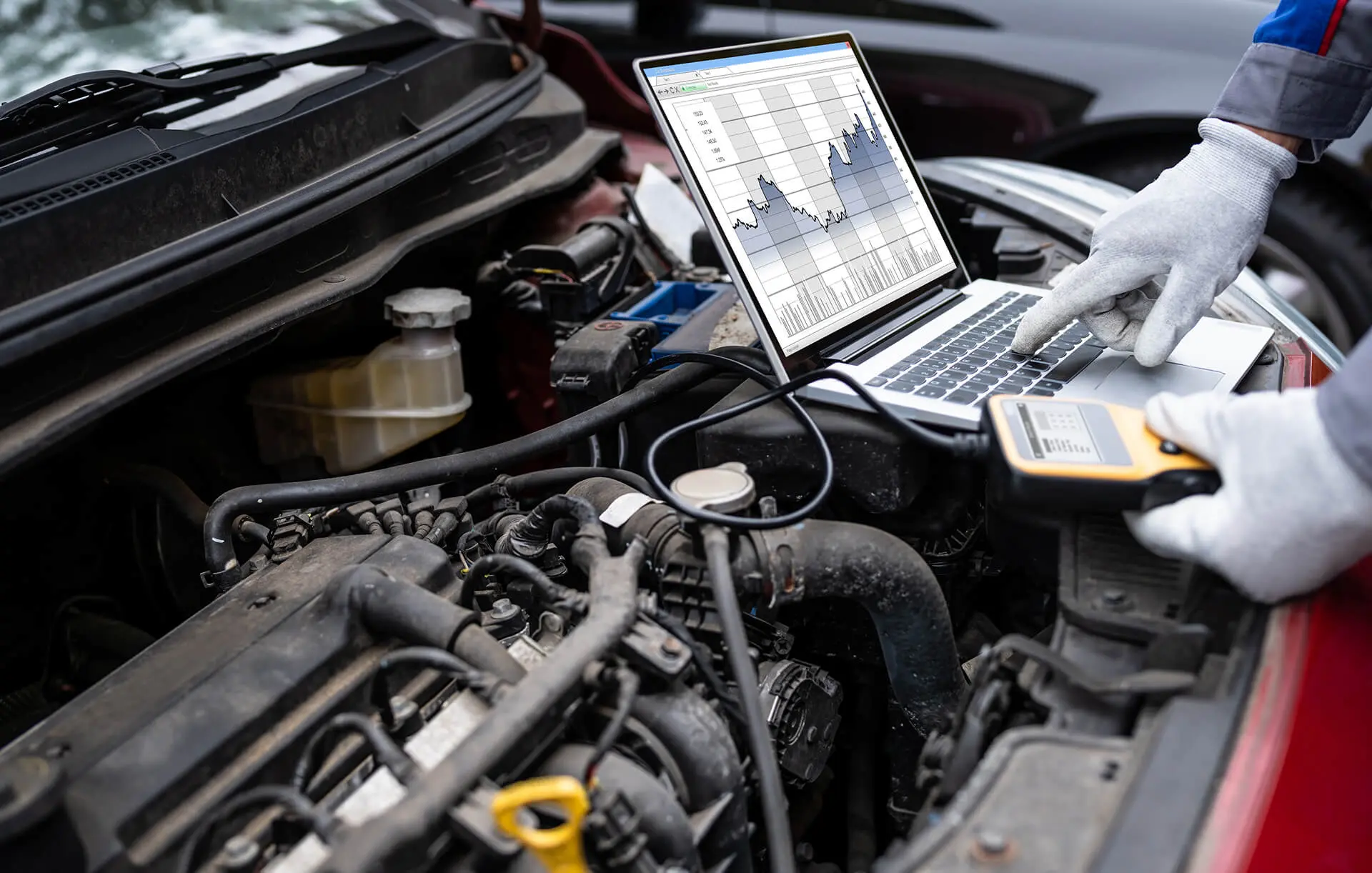 Mechanic diagnosing car engine with laptop.