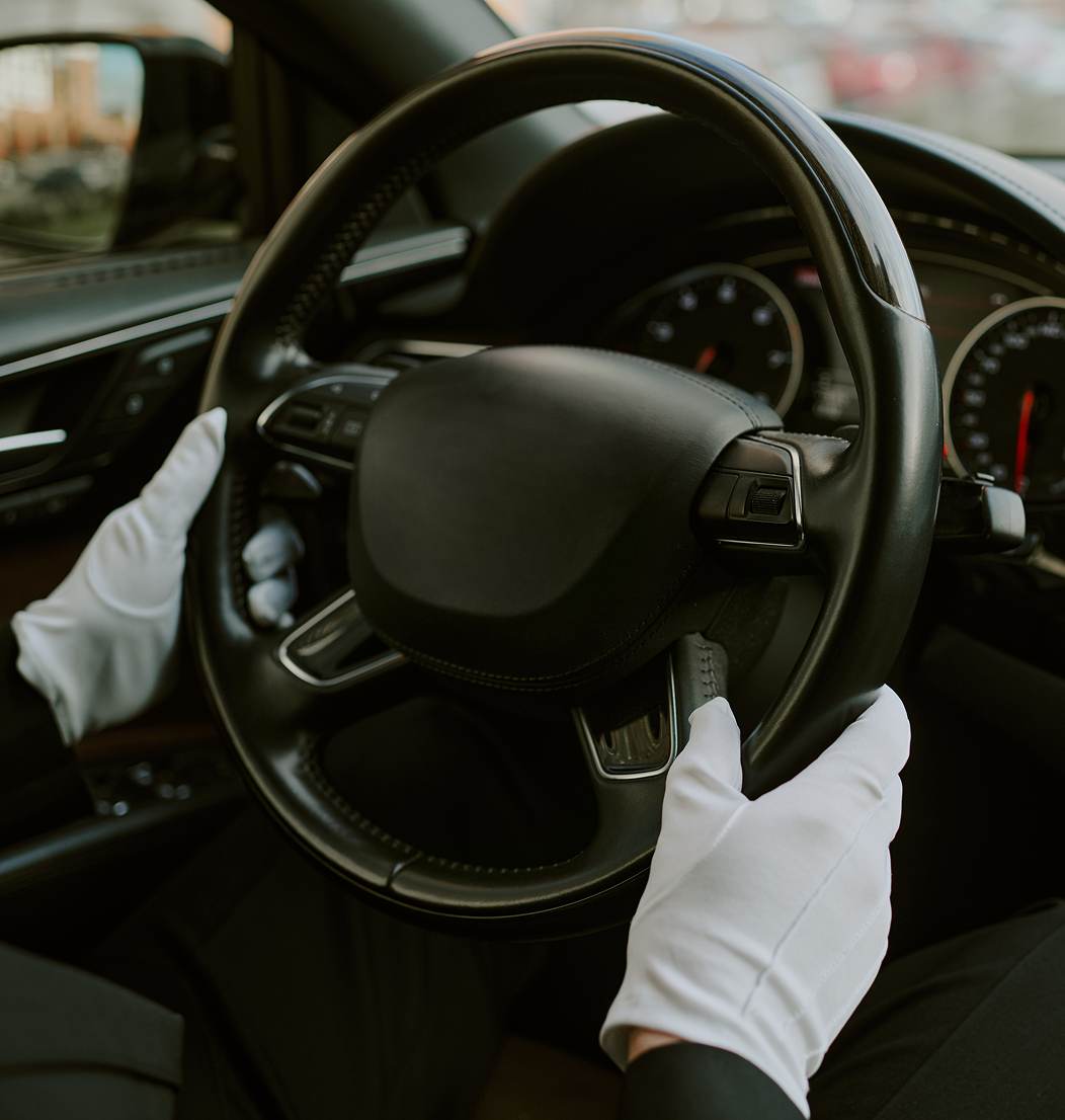 Driver with white gloves holding steering wheel.