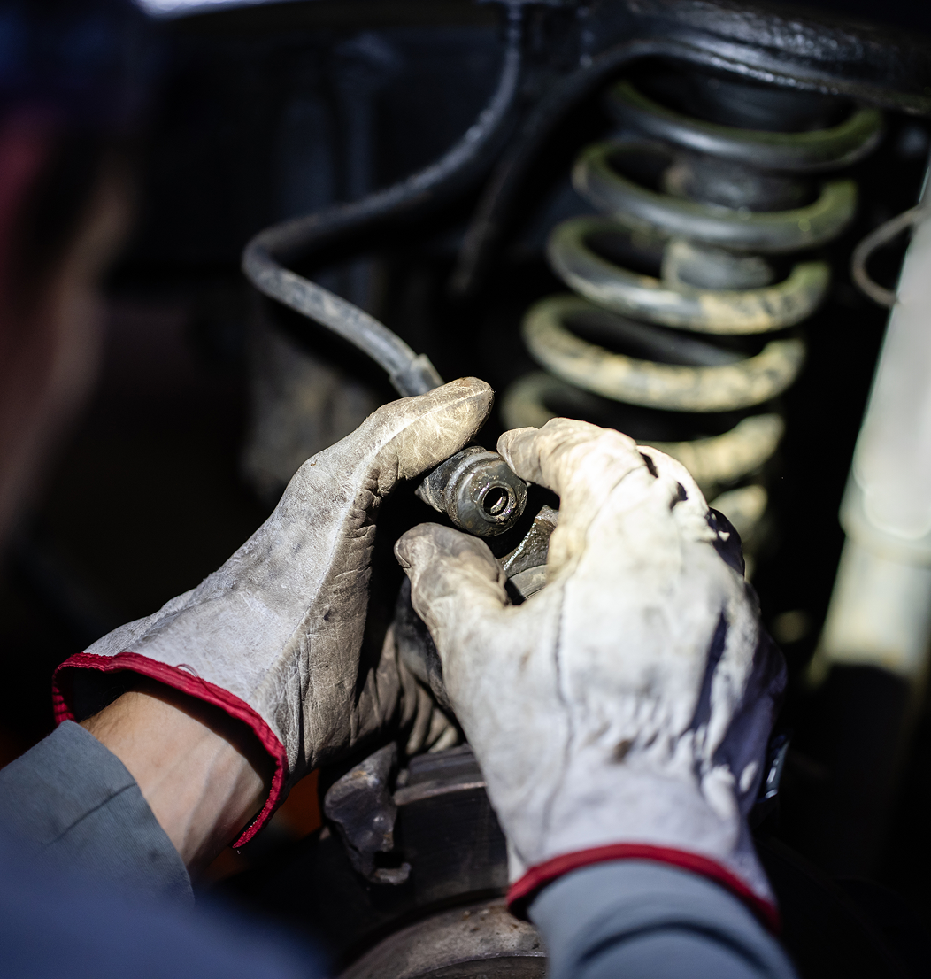 Mechanic working on car suspension with gloves.