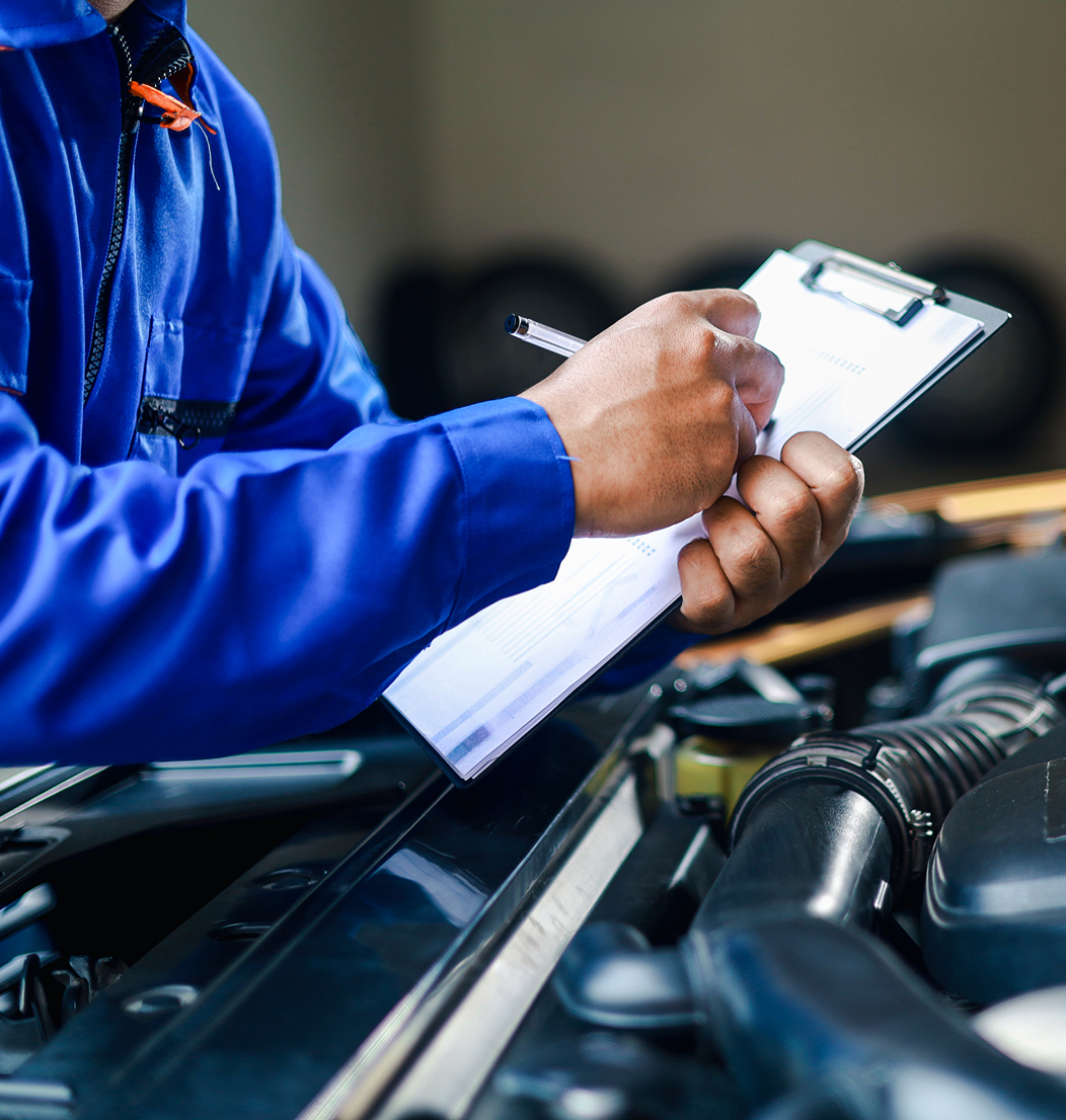 Mechanic writing on clipboard near car engine.