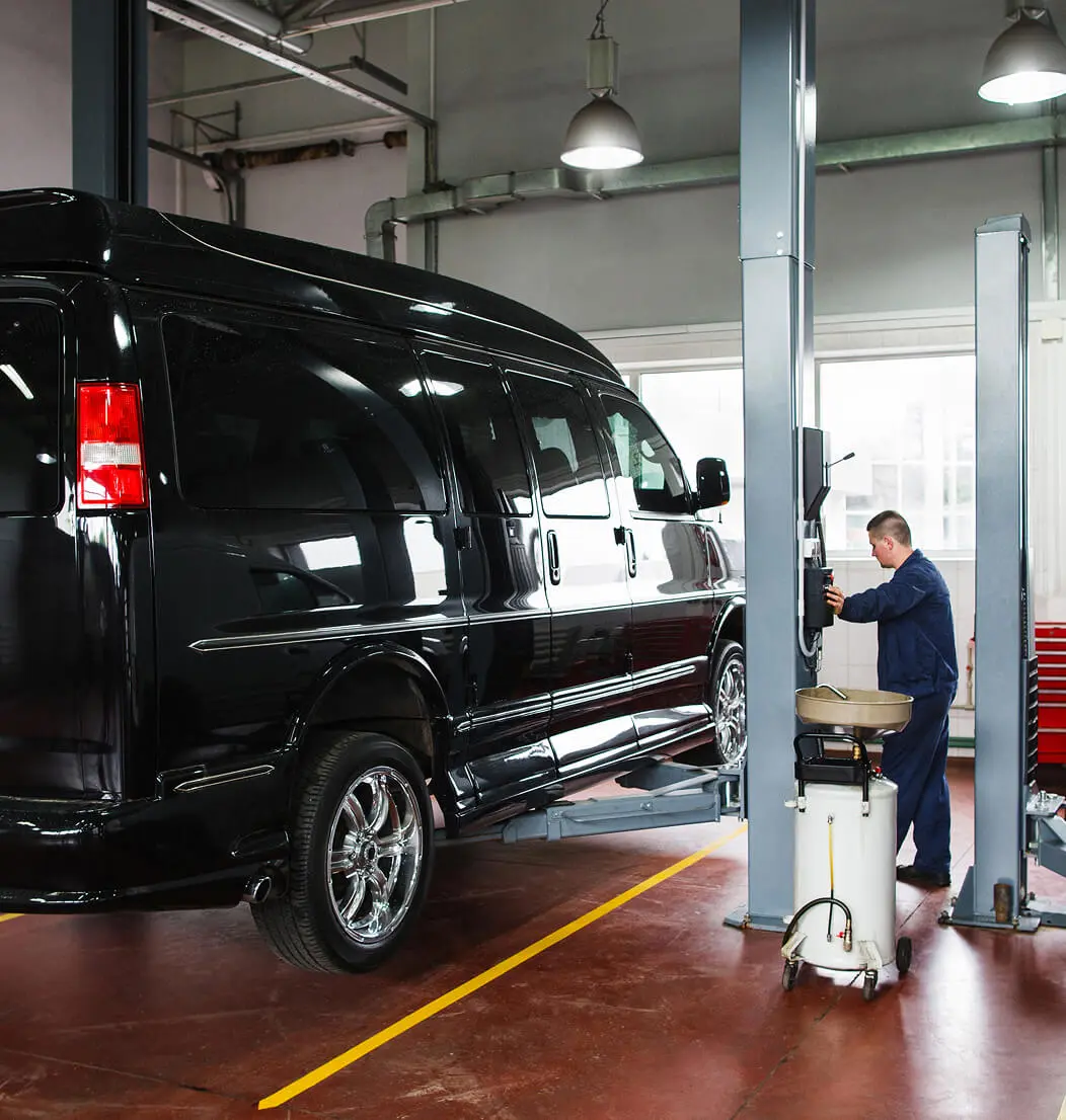 Mechanic inspecting black van on hydraulic lift.
