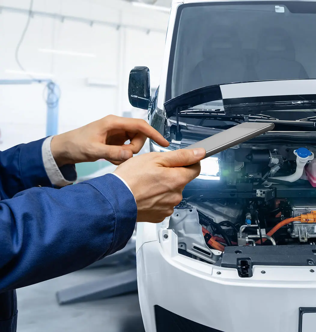 Mechanic inspecting car engine with tablet.
